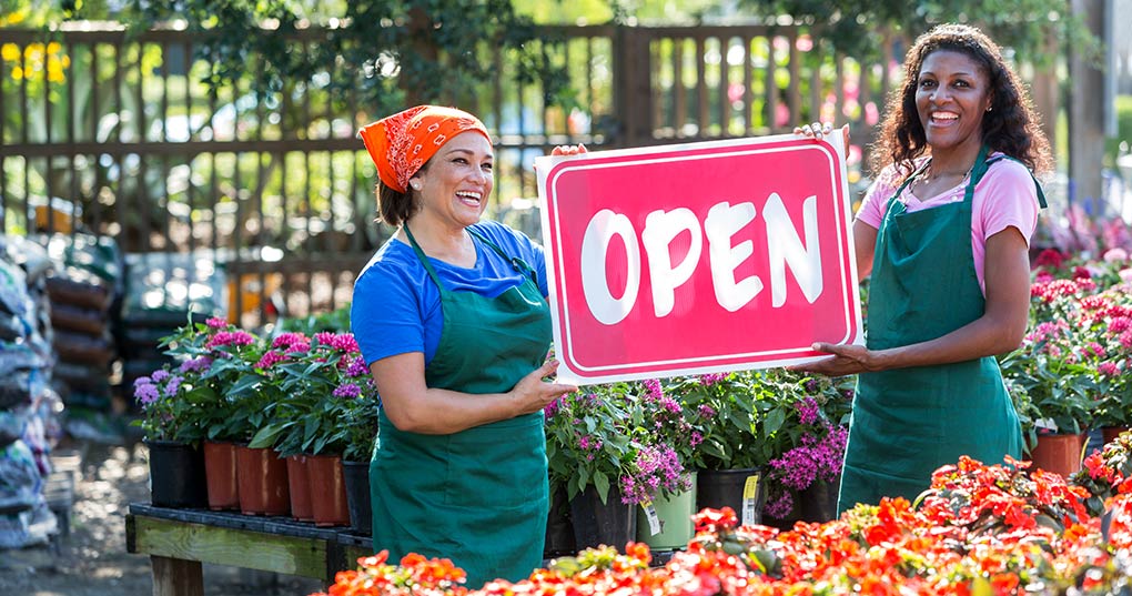 Two women holding an open sign at nursery.